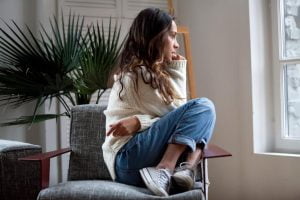 young woman seated anxiously in chair with legs drawn up under her and hugging herself wondering what are the signs of relapse