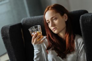 a woman stares at a drink possibly wondering why rates of alcohol consumption in women are rising